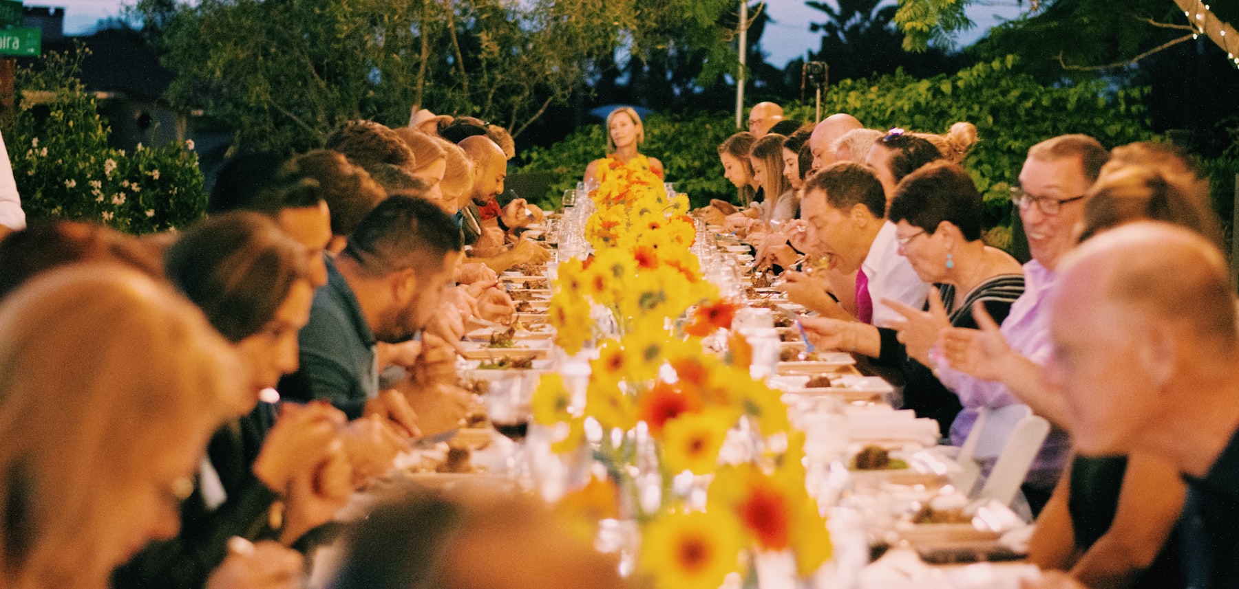 Guests dining at a long table dressed with a floral runner