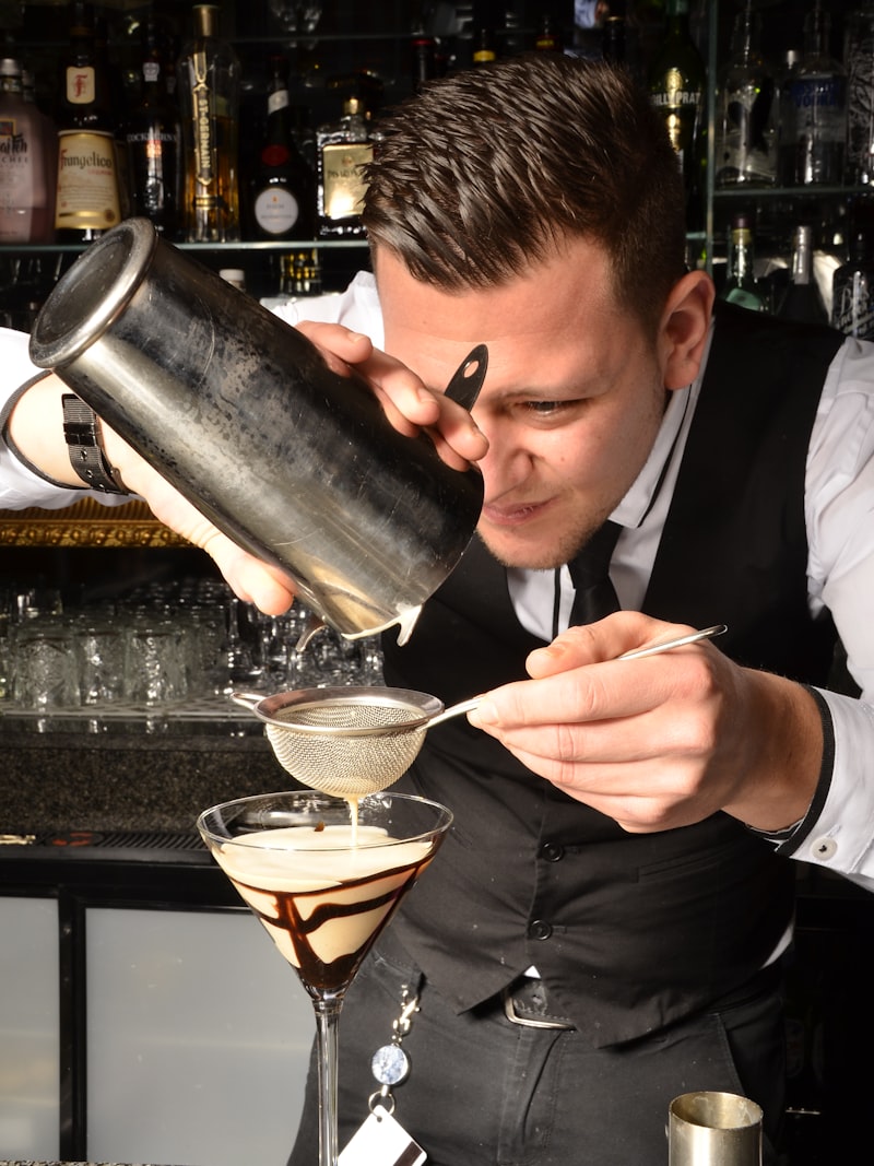 A bartender in a vest building a cocktail at the bar