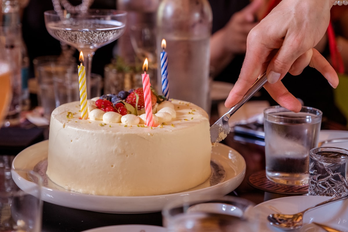 Hands reaching in around a candlelit birthday cake