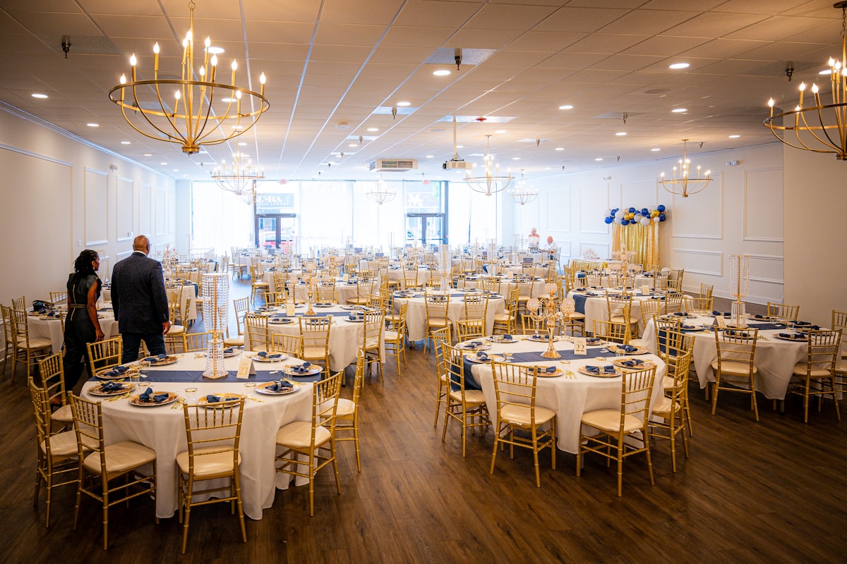 A banquet room of round tables set under chandeliers before doors open
